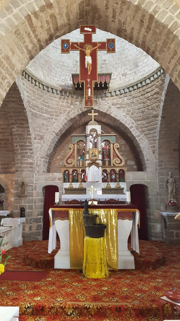 "Chapel with religious cross and alter with yellow and white fabric within a stone building."